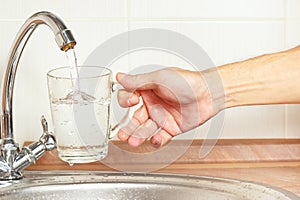 Hands pour water into the glass under the tap in kitchen