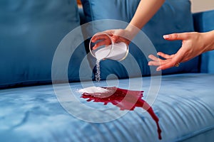hands pouring salt on fresh wine stain on blue sofa