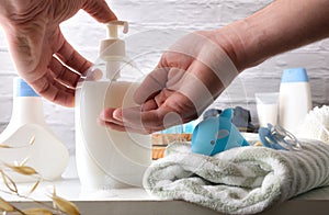 Hands pouring soap for the baby's bath on white furniture with accessories and products for the bath and shower