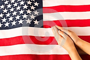 Hands of praying little girl on the background of the American flag. The concept of patriotism