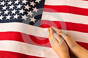 Hands of praying little girl on the background of the American flag. The concept of patriotism