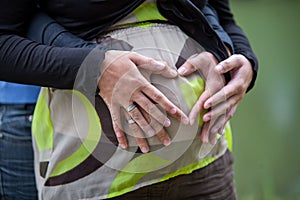 hands of pregnant woman and her female partner in heart shape on her belly