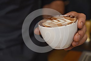 Hands presenting delicious coffee with milk cream decorating foam on mug