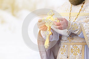 The hands of a priest dip an  Orthodox gold cross into the river. Feast of the Epiphany of Russia