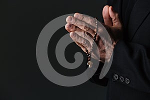 Hands of priest holding rosary and praying