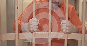 hands of prisoner in orange uniform hold the bars of the prison cell. close-up.