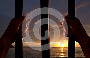 Hands of the prisoner with the sunset in the background