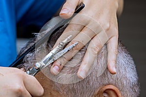 Hands of a professional barber with scissors and comb combs the hair of a man