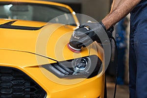 Hands of professional car service worker, with orbital polisher, polishing yellow luxury car hood
