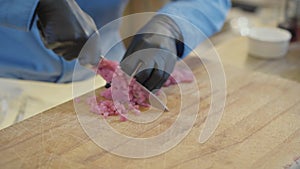 Hands of professional cook in black rubber gloves cutting meat with big sharp knife close up in the restaurant kitchen
