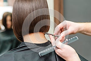 Hands of professional hair stylist is cuting hair tips with scissors and comb