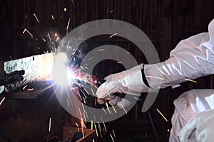 Hands of professional industrial welder with torch and protective gloves welding metal steel with spark in the factory.