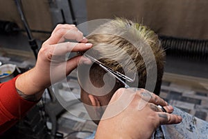 The hands of a professional male hairdresser with scissors and a comb cut the hair of a salon client at work