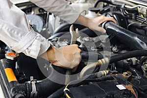 Hands of professional mechanic man in white uniform with wrench repairing engine of motor under car hood. Insurance concept.