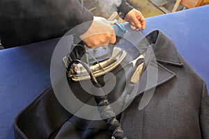 Hands of professional tailor ironing textile with steaming