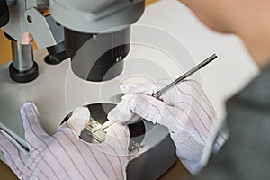 Hands of professional tech repairing small computer components on microscope table. Closeup. Electronics repair and fix