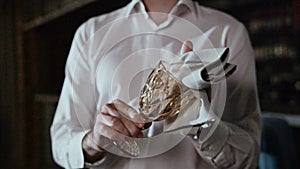 The hands of a professional waiter are wiping a glass glass with a gray cloth.