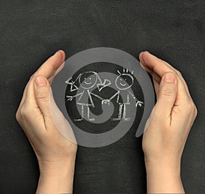 Hands protect children drawn on blackboard with chalk. Concept for International Children`s Day, June 1
