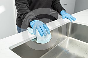 Hands in protective glove cleaning a modern sink with rag