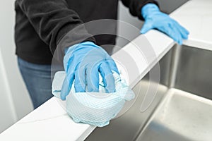 Hands in protective glove cleaning a modern sink with rag