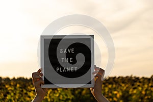 Hands of protester with text SAVE THE PLANET on black board on background of sunflower field. Reuse reduce recycle