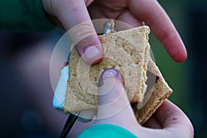 Hands pulling a marshmallow off a skewer to make a smore