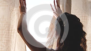 Hands pulling a window curtain for warm morning light. Slow motion. Young woman opening curtains in a bedroom. Closeup