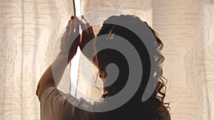 Hands pulling a window curtain for warm morning light. Slow motion. Young woman opening curtains in a bedroom. Closeup