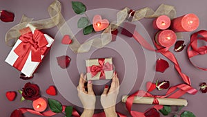 Hands put wrapped gift box with tied red ribbon bow for St. Valentine`s Day. Woman is preparing present gift for 14th of February