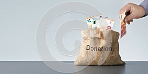 Hands putting 10 Euro banknote in donation bag with money with copy space. Banner.