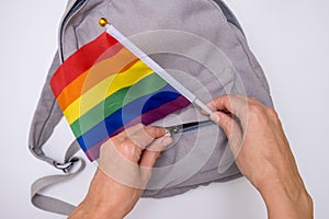 Hands putting an LGBT gay pride rainbow flag in a pocket of a backpack, pride parade preparations concept