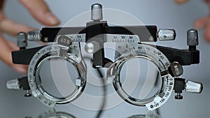 Hands putting optical trial frame on table, ophthalmic testing device close-up