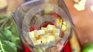 Hands putting pieces of pineapple in blender