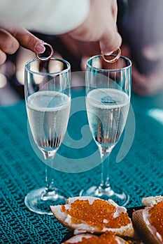 Hands putting rings in wedding glasses with sparkling champagne