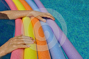 Hands on rainbow pool noodles in swimming pool