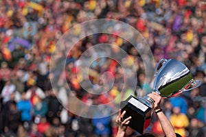 Hands raising trophy cup with unfocused spectators background