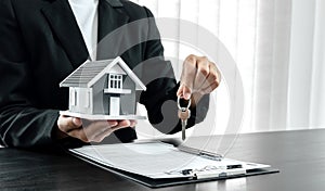 The hands of the real estate agent are holding the keys along with the house insurance contract documents and samples of the house
