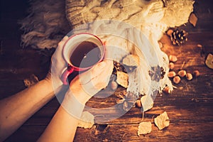 Hands in red knitted gloves holding a hot cup of coffee against yellow leaves background. Concept of autumn time, warmth and cozin