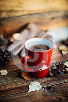 Hands in red knitted gloves holding a hot cup of coffee against yellow leaves background. Concept of autumn time, warmth and cozin