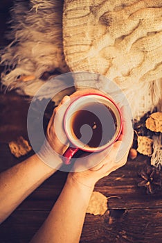 Hands in red knitted gloves holding a hot cup of coffee against yellow leaves background. Concept of autumn time, warmth and cozin