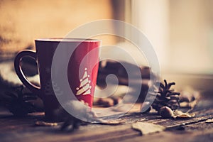 Hands in red knitted gloves holding a hot cup of coffee against yellow leaves background. Concept of autumn time, warmth and cozin