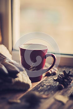 Hands in red knitted gloves holding a hot cup of coffee against yellow leaves background. Concept of autumn time, warmth and cozin