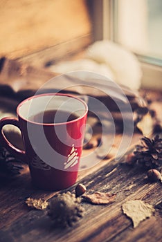 Hands in red knitted gloves holding a hot cup of coffee against yellow leaves background. Concept of autumn time, warmth and cozin