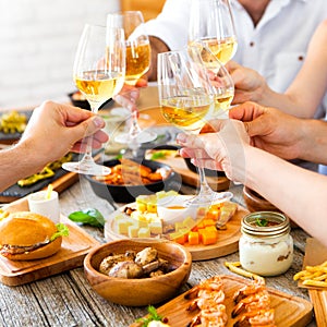 Hands with red wine toasting over served table with food.