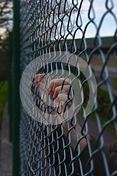 Hands of a refugee woman on a wire fence