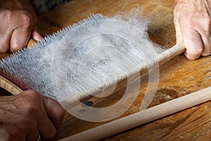 hands removing carded raw wool from a carding board with a round stick, on wooden surface photo