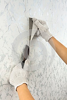 Hands removing old wallpaper with spatula