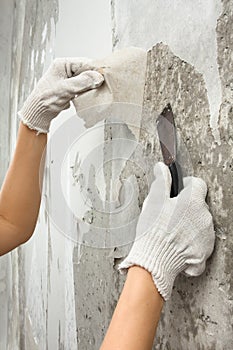 Hands removing old wallpaper with spatula during repair