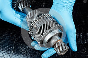 Hands of a repairman in blue gloves hold gears, close-up. Repair box predach, repair of used cars. Metal background