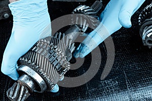 Hands of a repairman in blue gloves hold gears, close-up. Repair box predach, repair of used cars. Metal background